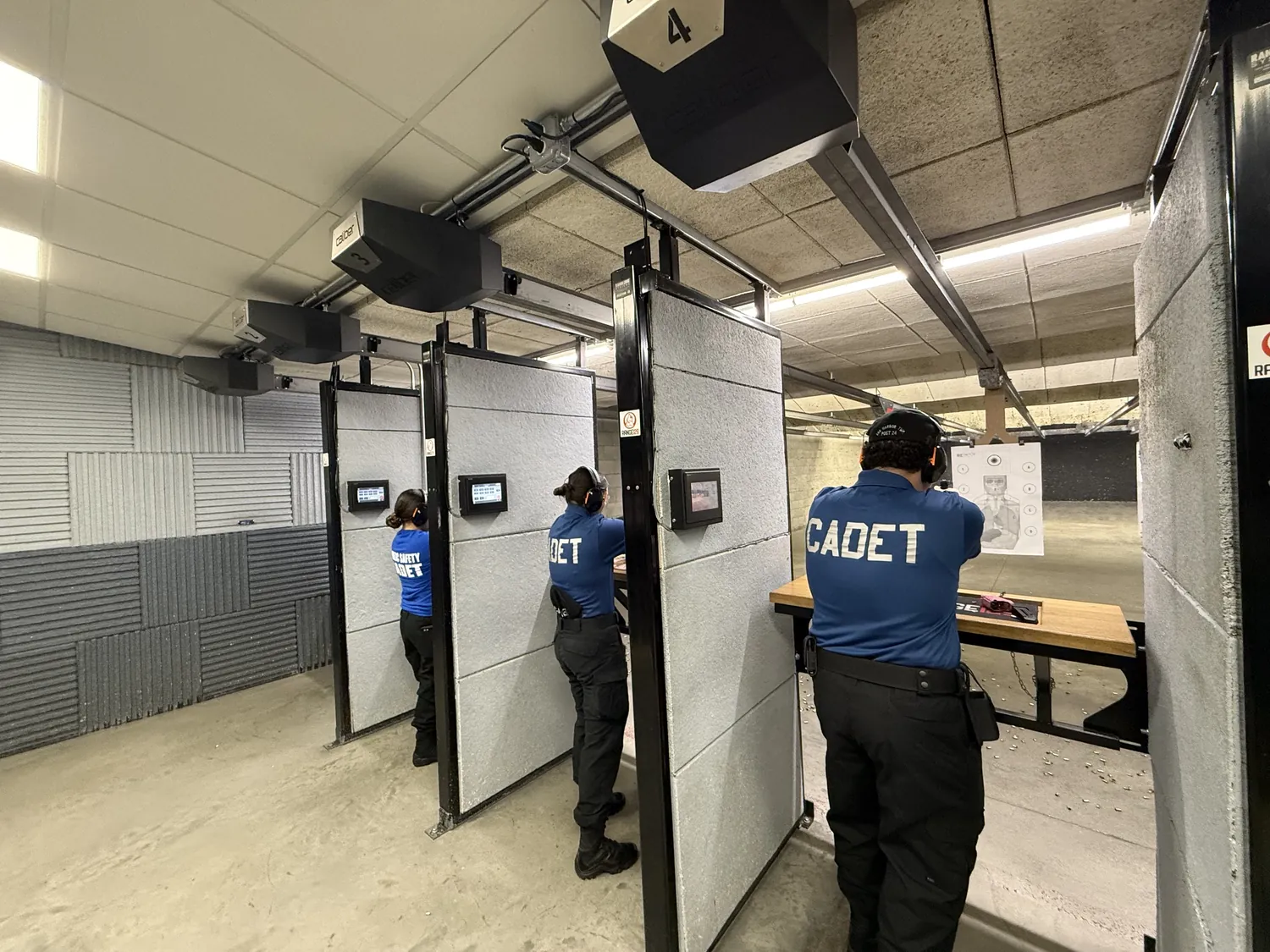 Cadets in blue shirts training at an indoor shooting range